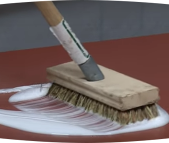 A brush scrubbing a white paint like substance onto flooring