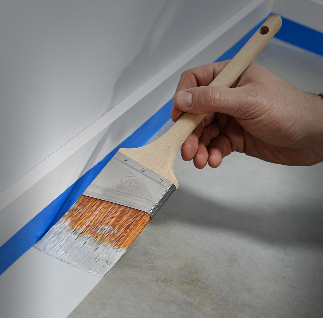 Mobile-sized image pf person painting a concrete floor along baseboard.