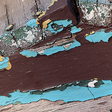 Close up image of a wood with peeling paint and underneath is another coat of a different color.