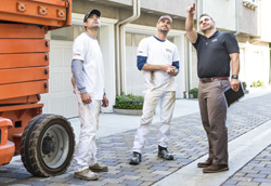 A full body view of a BEHR PRO Rep pointing at a building while a 2 Pro Painters are looking at what he is pointing.