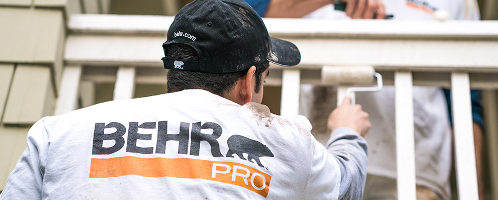Small A close up image of a back of a painting contractor who is painting with a roller with the logo of BEHR PRO imprinted on the shirt