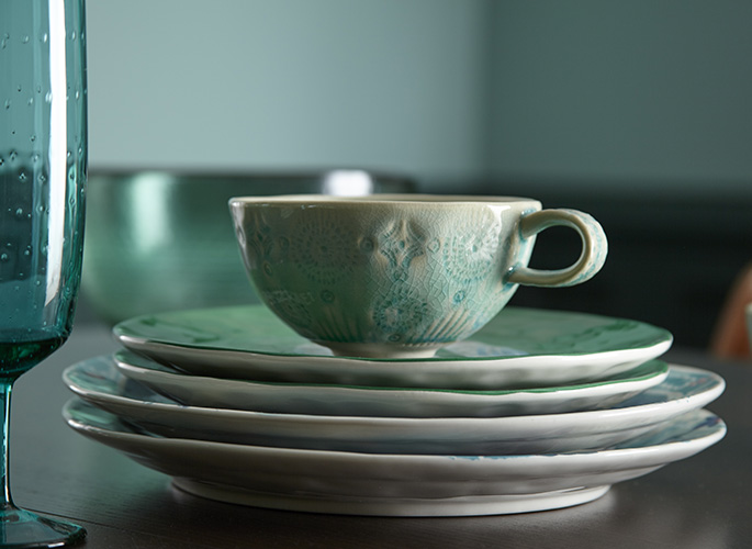 A tight crop of blueish-green plates stacked with a tea cup on top of them ready for a calming evening.