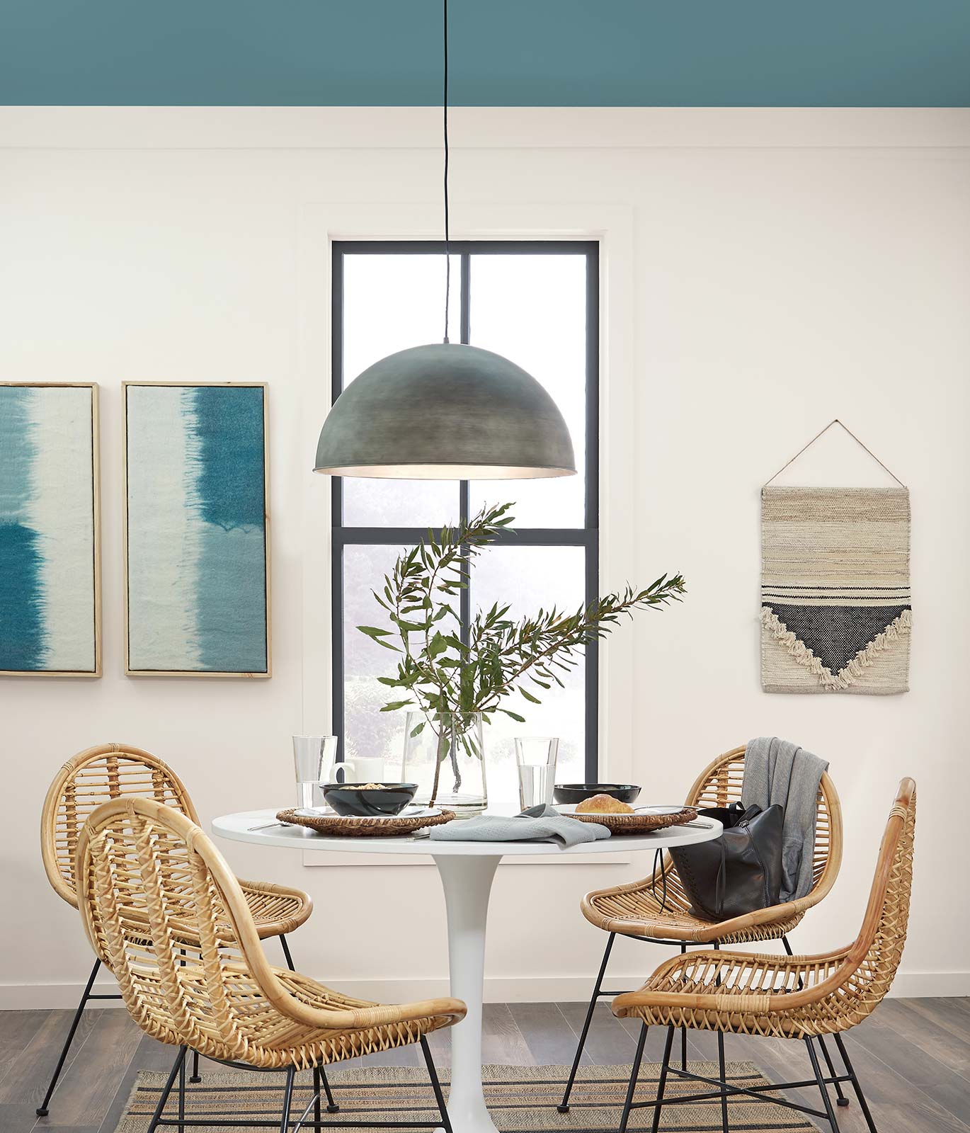 A casual dining area with a small round table and four rattan chairs surrounding it. Wall is painted in white with a blue painted ceiling. The atmosphere is relaxed and calm.
