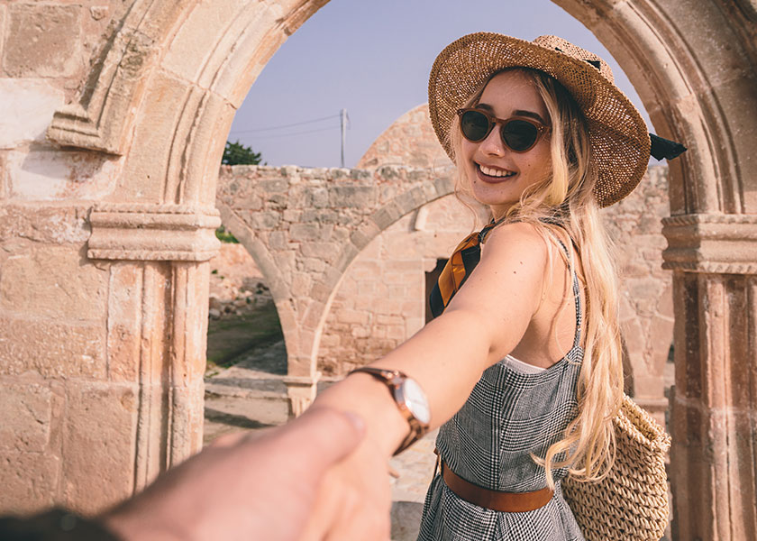 A woman with a smile on her face greeting someone and looking like she is using her hand to pull him closer to her.