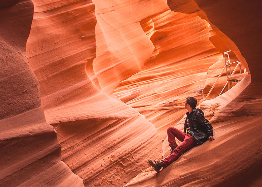 A person sitting inside a canyon. Rocks colored in bright orange and brown hues surround him.