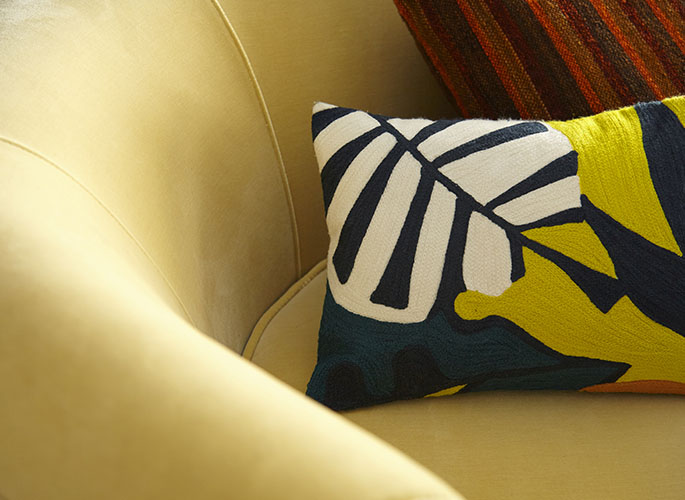A tight crop of a yellow couch with bright yellow and navy blue abstract pattern on the pillows.