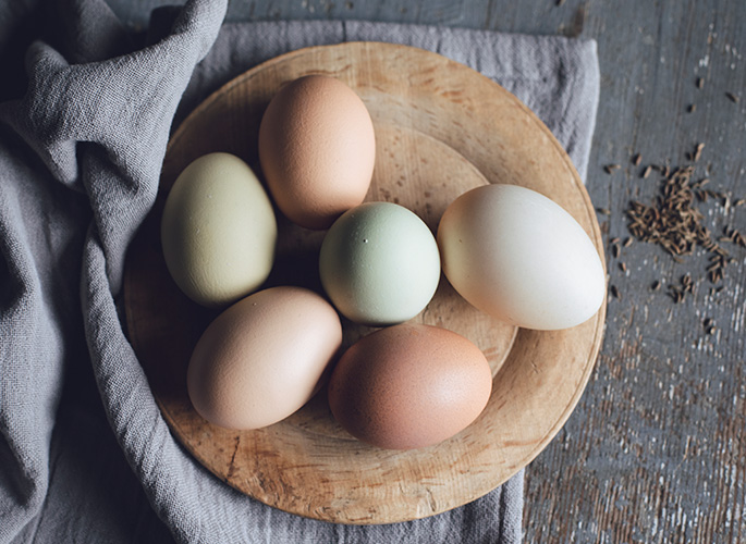 Ceramic eggs painted in subtle pastel colors sitting in a nest made of carved wood. 