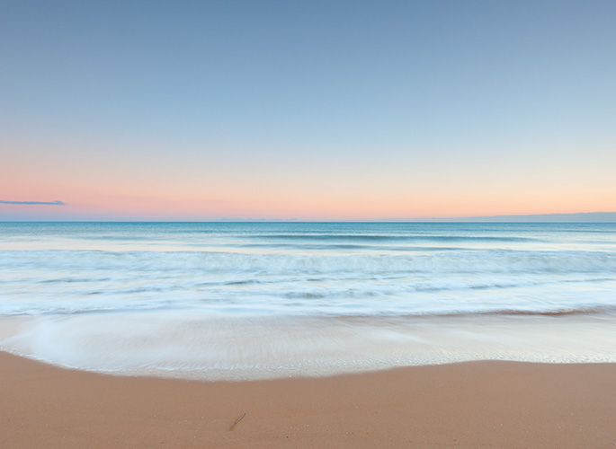 An ocean scene showing with the subtle colors of the sun rising painted in the background. 