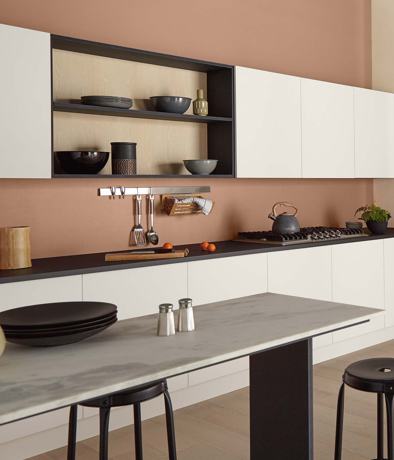 A kitchen painted in a burnt orange color with white cabinets and a white long table. The décor is subtle letting the color of the walls stand out.